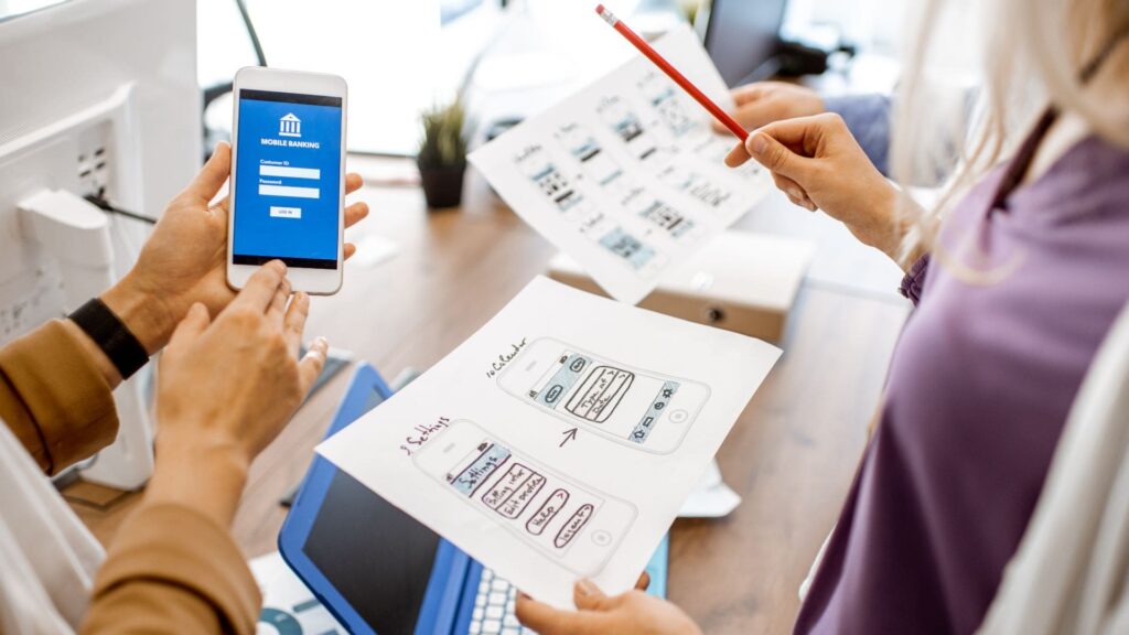 Duas mulheres estudando o desenvolvimento mobile através do papel em frente ao seu smartphone.